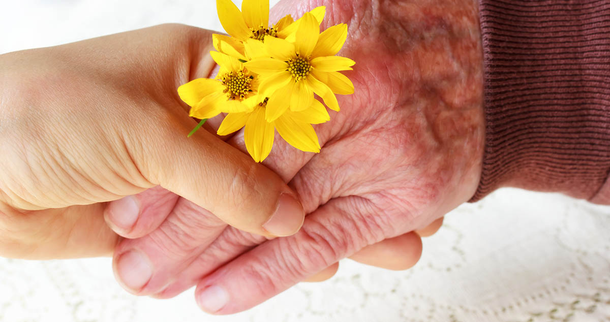 Senior hand holding younger hand with flowers